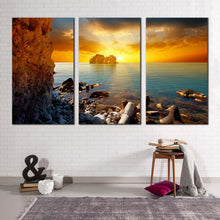 Load image into Gallery viewer, dramatic sunset canvas wall art blue sea ocean rocks boulders canvas set yellow sky stony beach 3 piece canvas print
