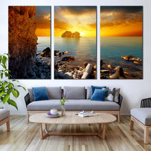 Load image into Gallery viewer, dramatic sunset canvas wall art blue sea ocean rocks boulders canvas set yellow sky stony beach 3 piece canvas print In Living Room
